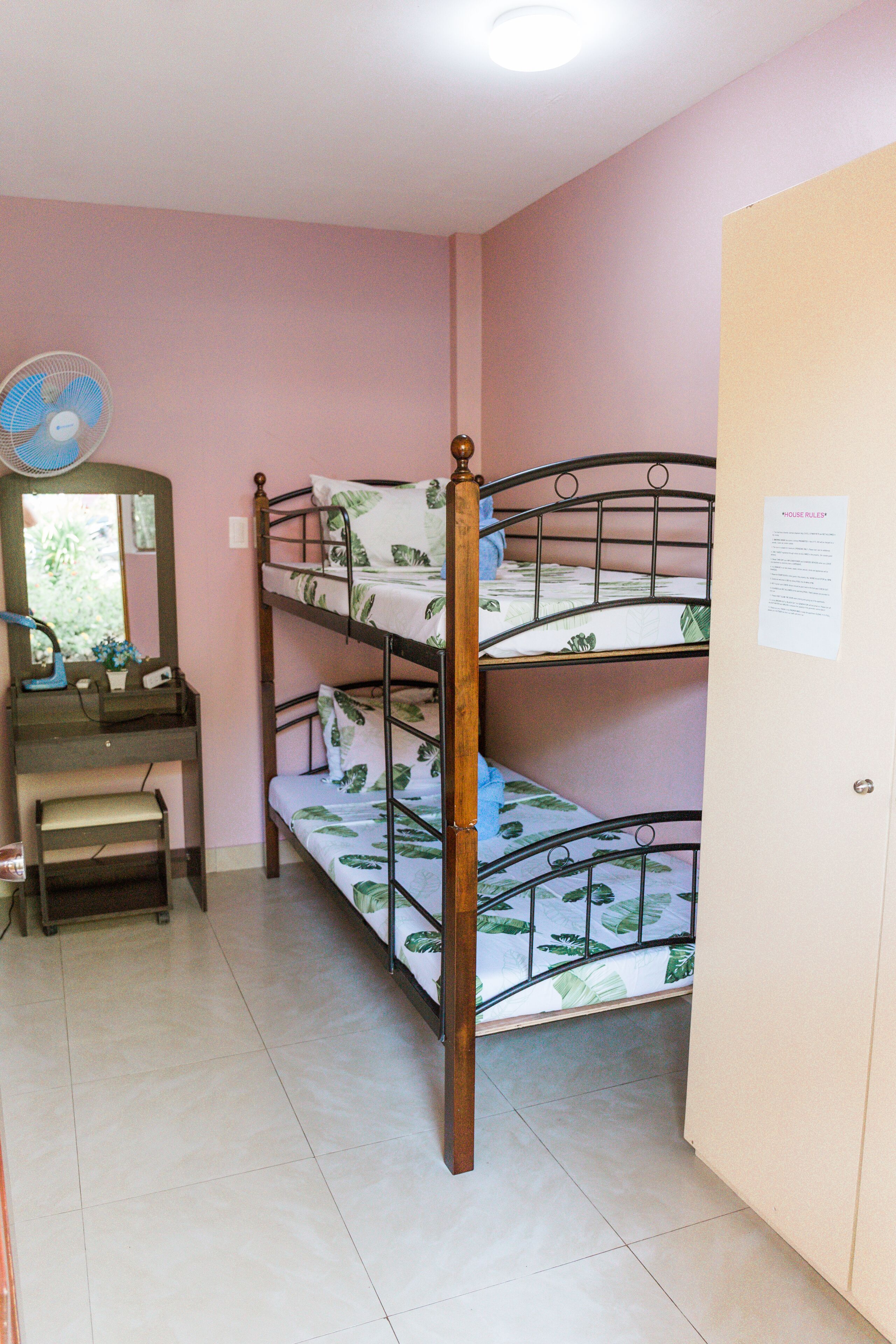 Habitación con literas, escritorio, silla, espejo y ventilador.