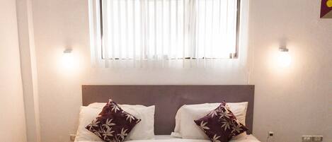 Un dormitorio con una cama, ventilador de techo, ventana con persianas y aire acondicionado.