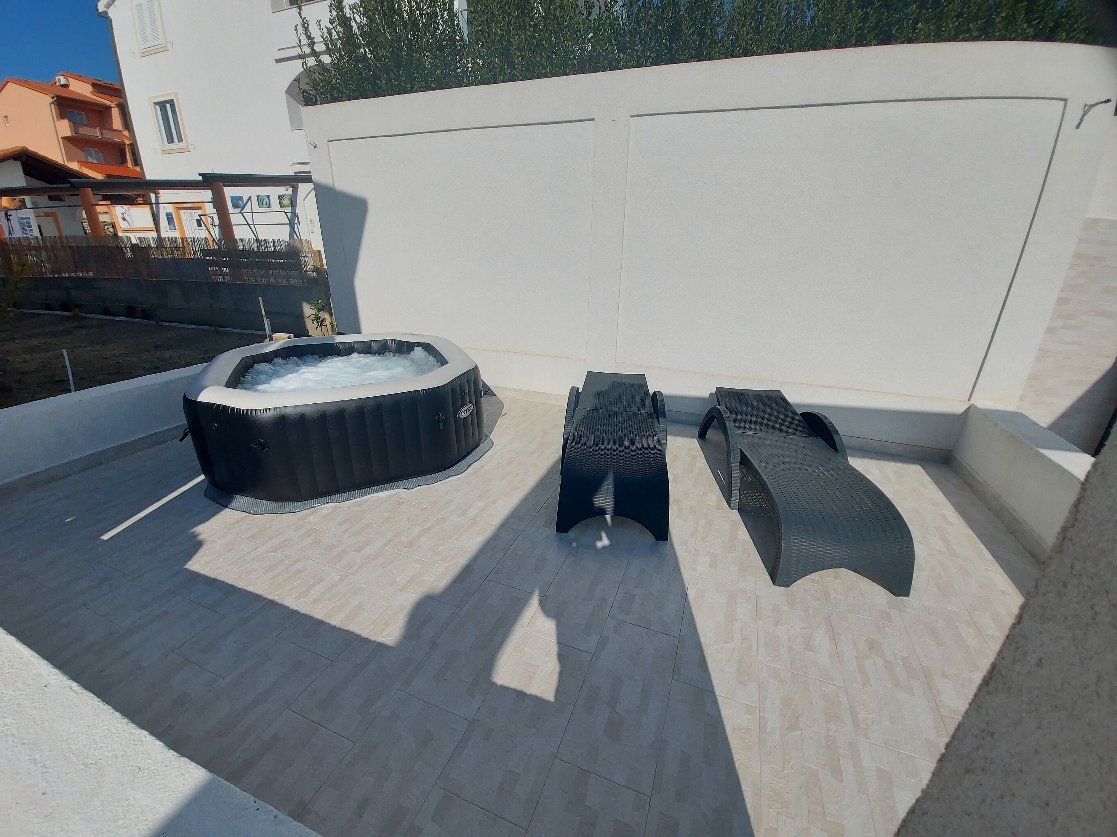 A rooftop terrace with a hot tub, two lounge chairs, and a tiled floor.