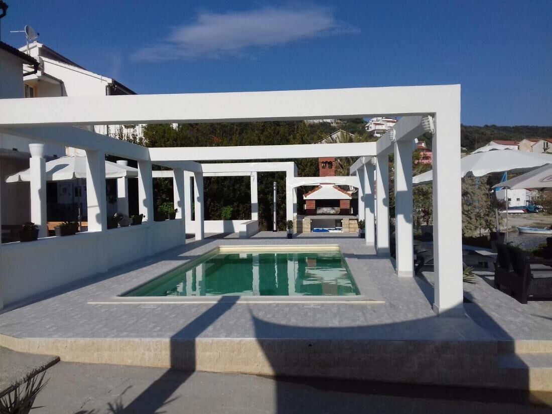 Un espace piscine extérieur moderne, doté d’une pergola blanche et entouré d’une terrasse dallée.