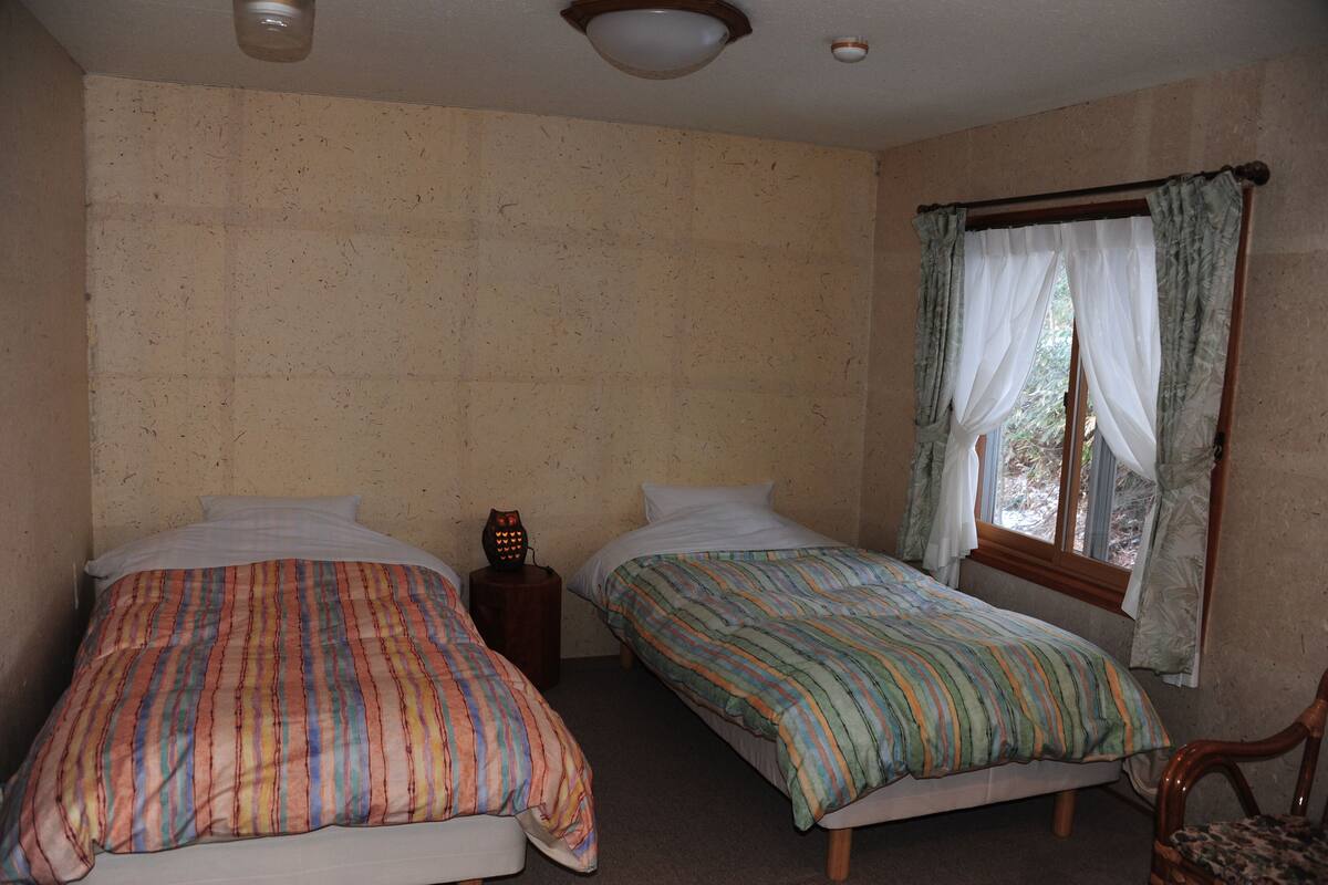 Una habitació amb dos llits, una tauleta de nit amb una làmpada i una finestra amb cortines.