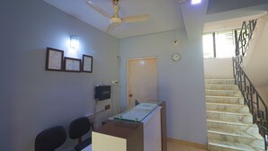 A room with a desk, chairs, a ceiling fan, framed certificates, a clock, and a staircase. - Bh Boutique Hotel (Baruipur)