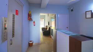 A hallway with a ceiling fan, a fire extinguisher, a door with a security camera, and a glass display case. - Bh Boutique Hotel (Baruipur)