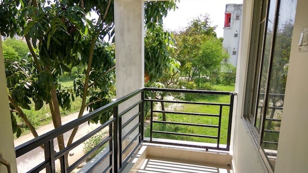 A balcony with a metal railing, a tiled floor, and a view of greenery and buildings in the background. - Bh Boutique Hotel (Baruipur)
