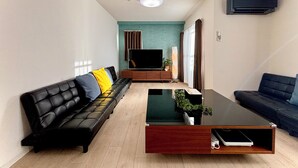 A modern living room with a black leather sofa, a wooden coffee table, and a flat-screen TV. - Wabi Sabi Osaka (Osaka)