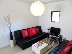 A modern living room with a black sofa, red cushions, a coffee table, a TV, and a large light fixture.