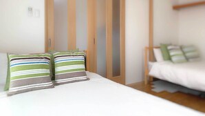 A bedroom with a bed, two pillows, a wooden wardrobe, and a bedside table. - Wabi Sabi Osaka (Osaka)