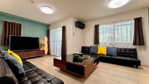 A modern living room with a sectional sofa, a flat-screen TV, a coffee table, and a large window with curtains. - Wabi Sabi Osaka (Osaka)