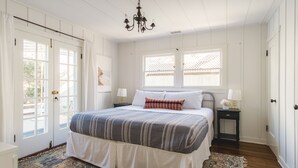 A bedroom with a bed, two bedside tables, a chandelier, a window, and a door.