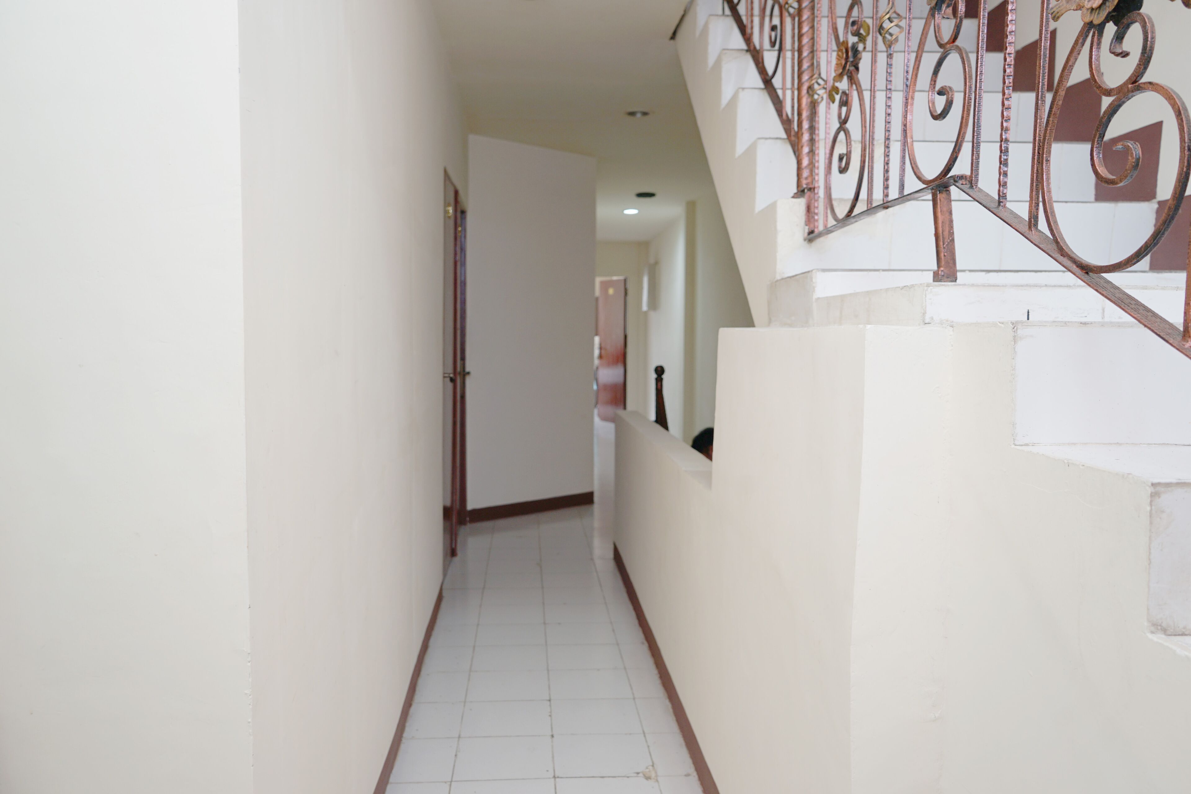 A narrow hallway with a staircase on the right, white walls, and a tiled floor.