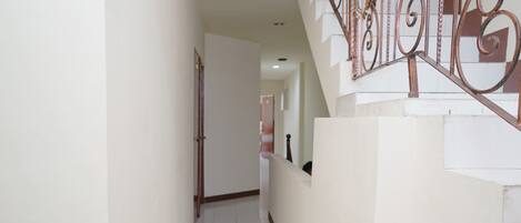 A narrow hallway with a staircase on the right, white walls, and a tiled floor.
