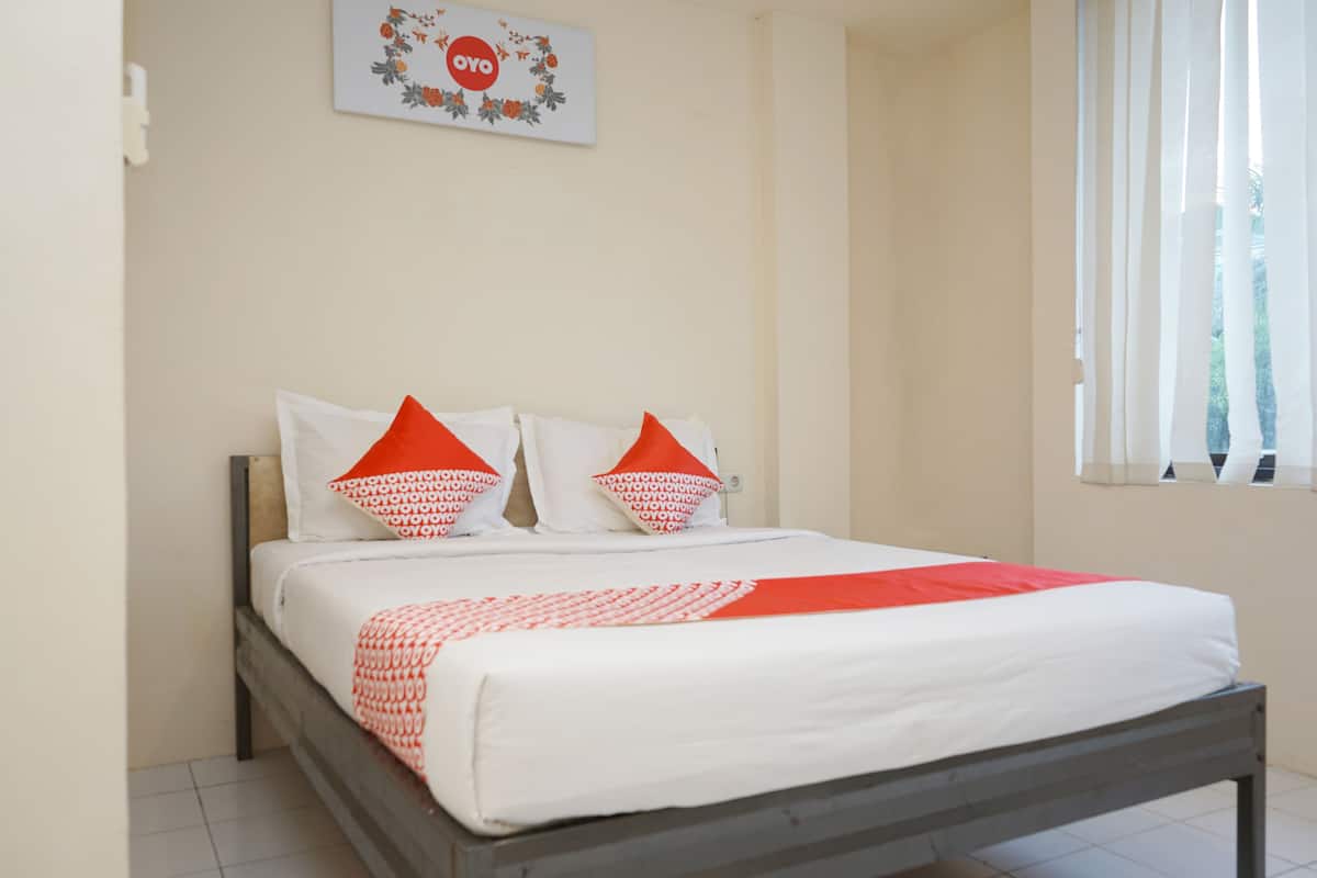 A neatly made bed with white and red bedding, two pillows, and a framed picture on the wall.