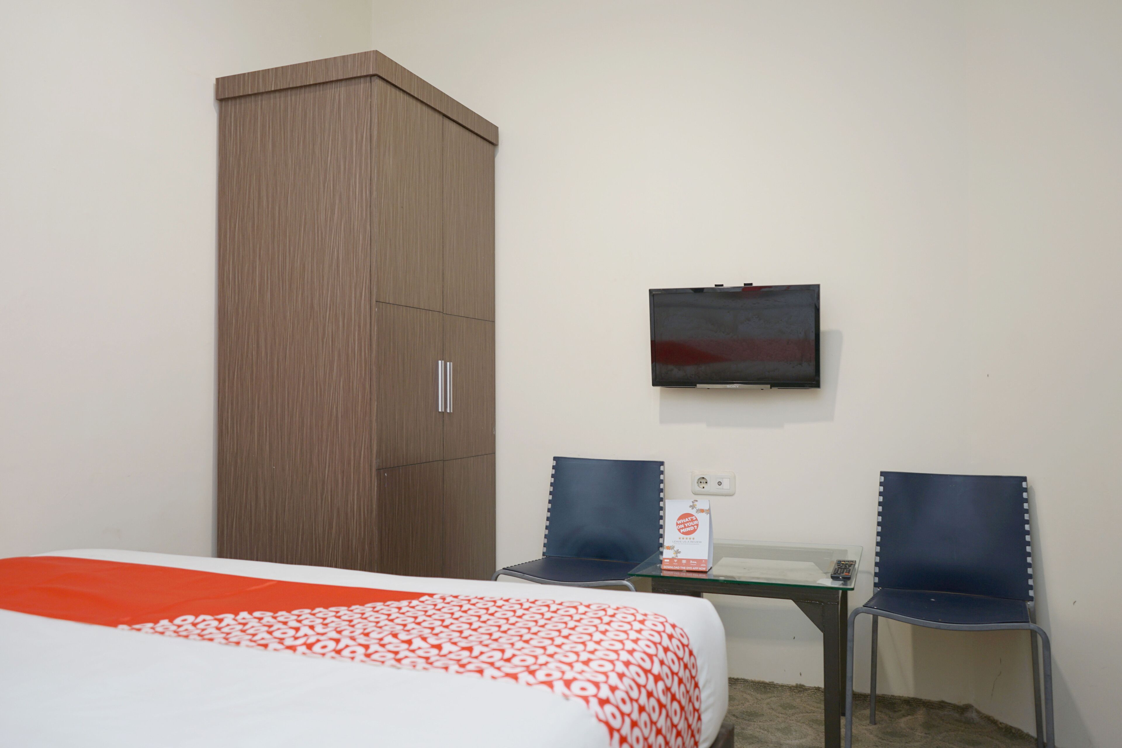 Ein Hotelzimmer mit Bett, Schrank, zwei Stühlen, einem kleinen Tisch und einem Fernseher an der Wand.
