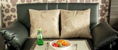 A sofa with two beige pillows and a bottle of beer on a table.