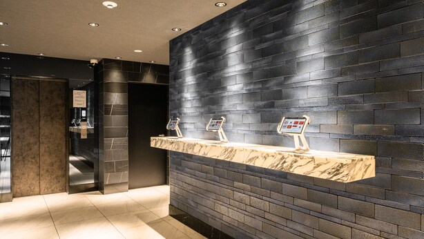 A modern bathroom with a black tiled wall, marble countertop, and two digital information kiosks.