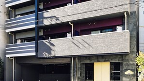 A multi-story building with a modern architectural design, featuring balconies and a ground-level entrance.