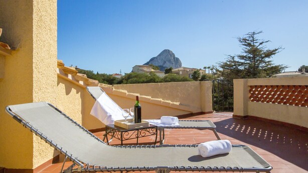 Une terrasse sur le toit avec deux chaises longues, une table avec une bouteille et des verres, et une vue sur une montagne.
