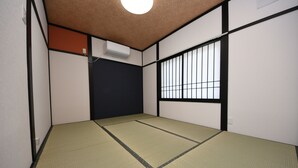 Una habitación tradicional con esteras de tatami, una puerta corredera, una ventana con barrotes negros y una lámpara en el techo.