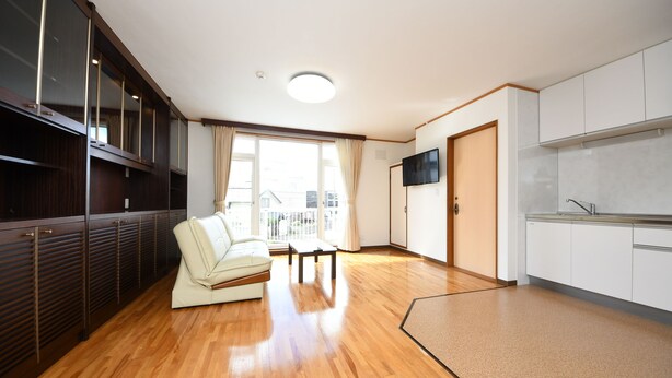 Un apartamento moderno con suelo de madera, un sofá, un televisor y una zona de cocina.