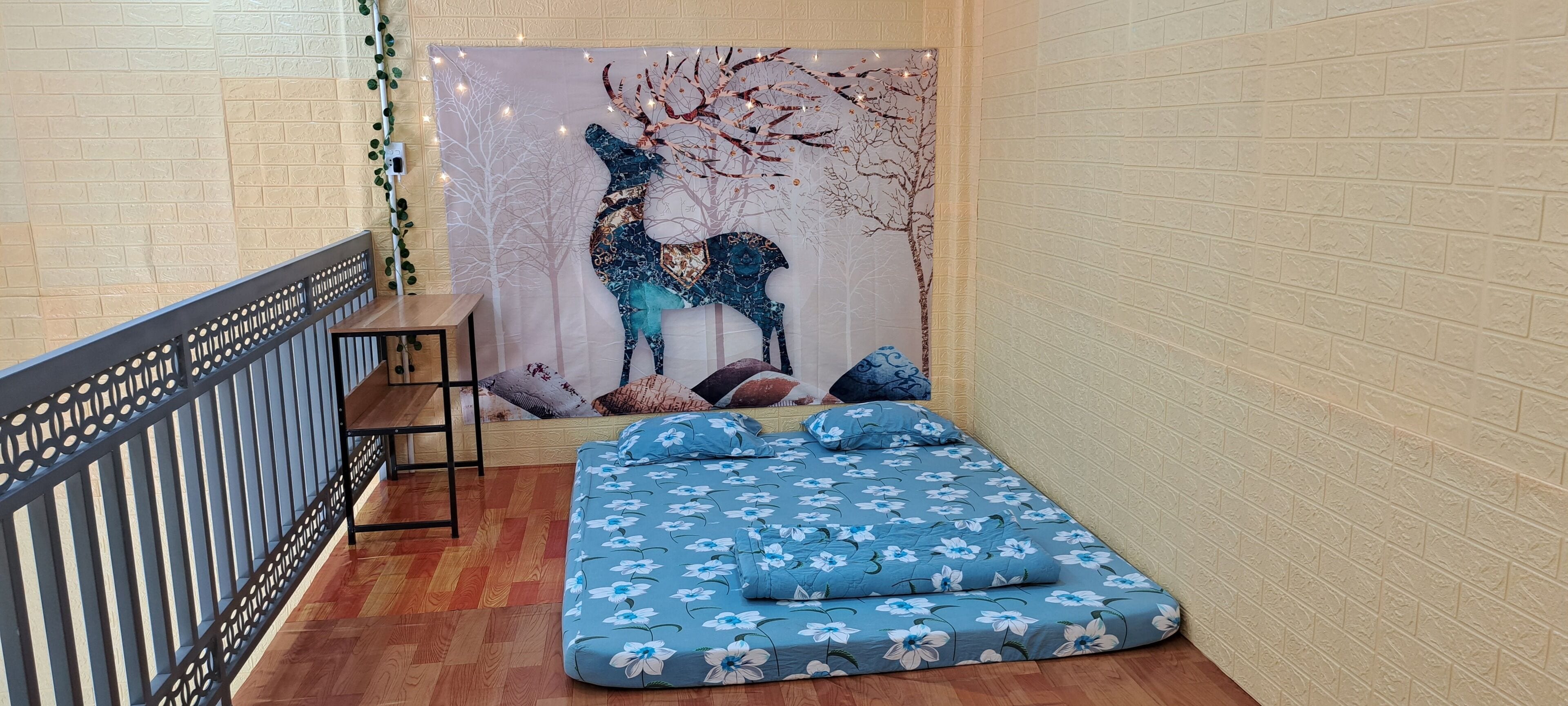 A cozy room with a blue floral bedspread, a decorative wall with a tree and deer, and a wooden bench.