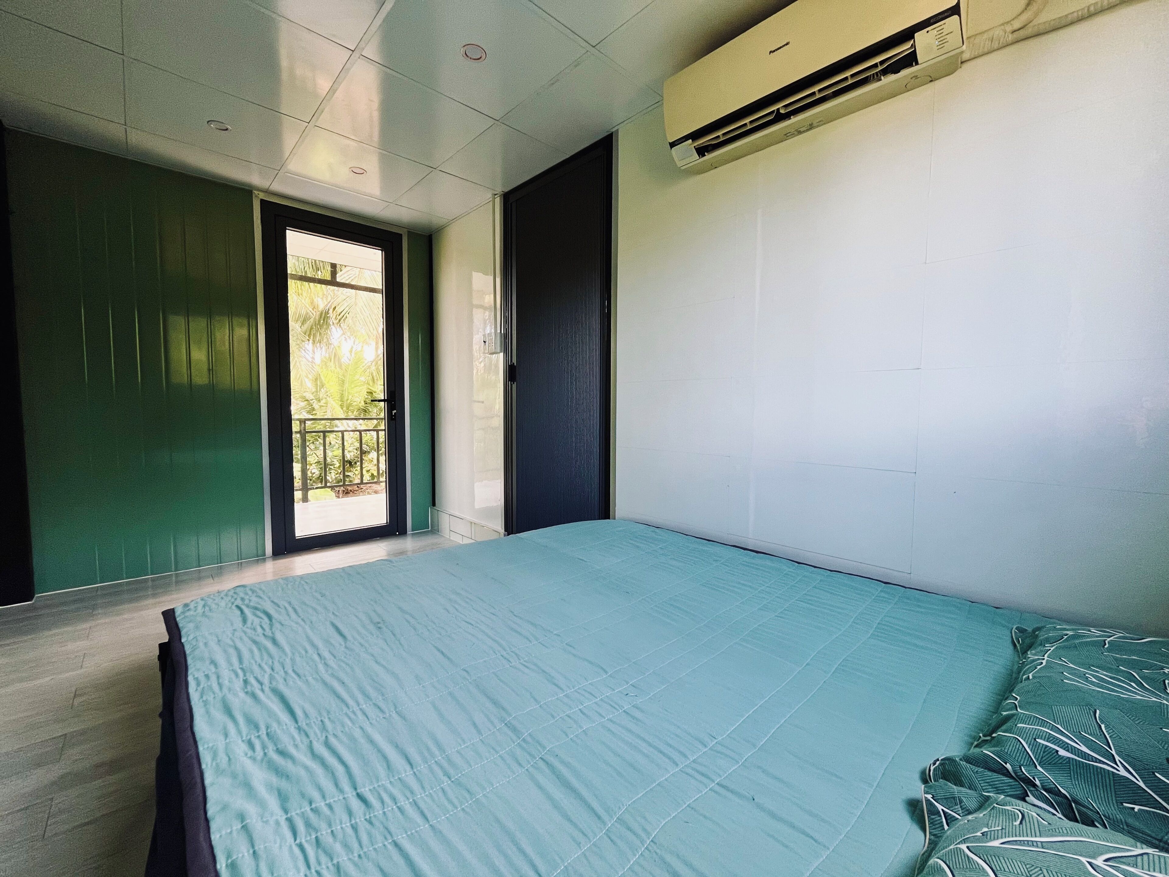 A bedroom with a bed, a sliding door to a balcony, and an air conditioning unit on the wall.