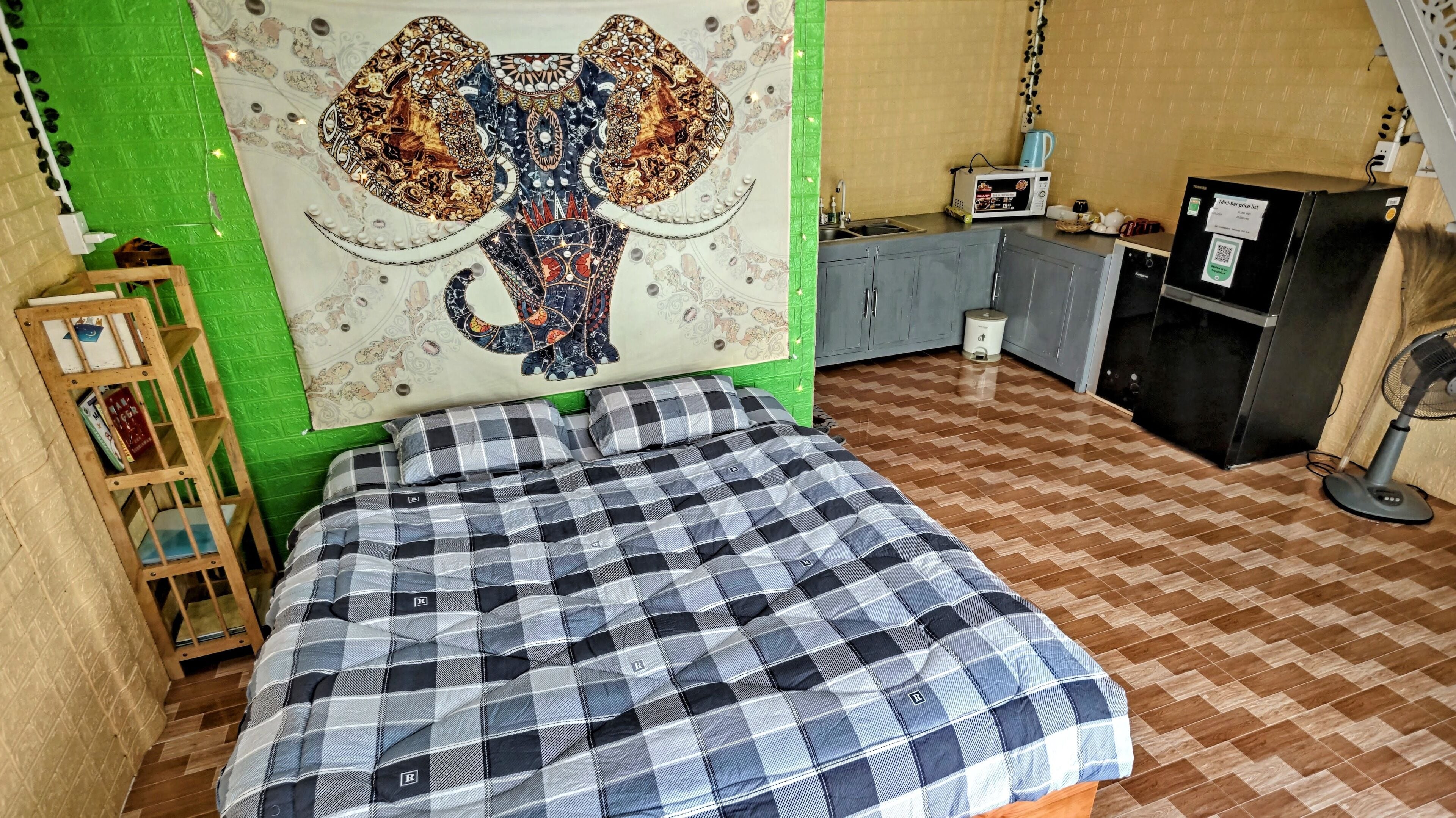 A room with a bed, a green wall, a patterned tapestry, a microwave, a refrigerator, and a small cabinet.
