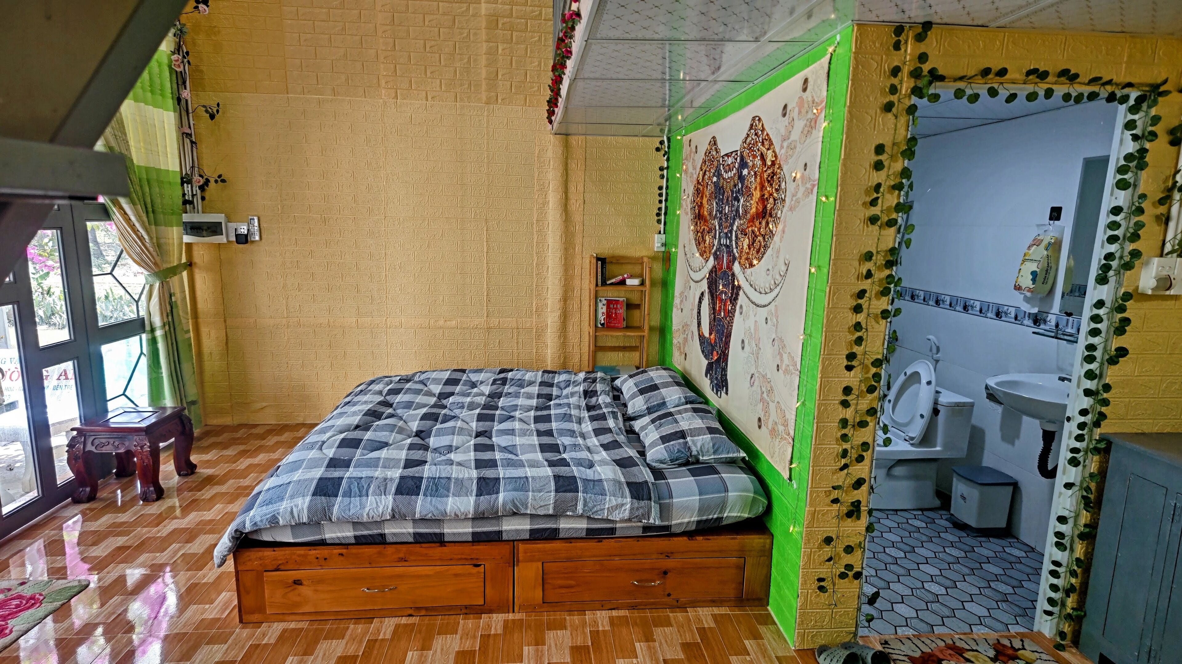 Una habitación con una cama de madera, una pared de acento verde, un baño con inodoro y lavabo, y una ventana con cortinas.