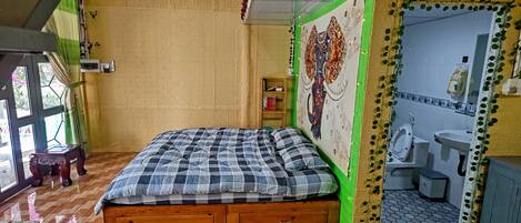 Una habitación con una cama de madera, una pared de acento verde, un baño con inodoro y lavabo, y una ventana con cortinas.
