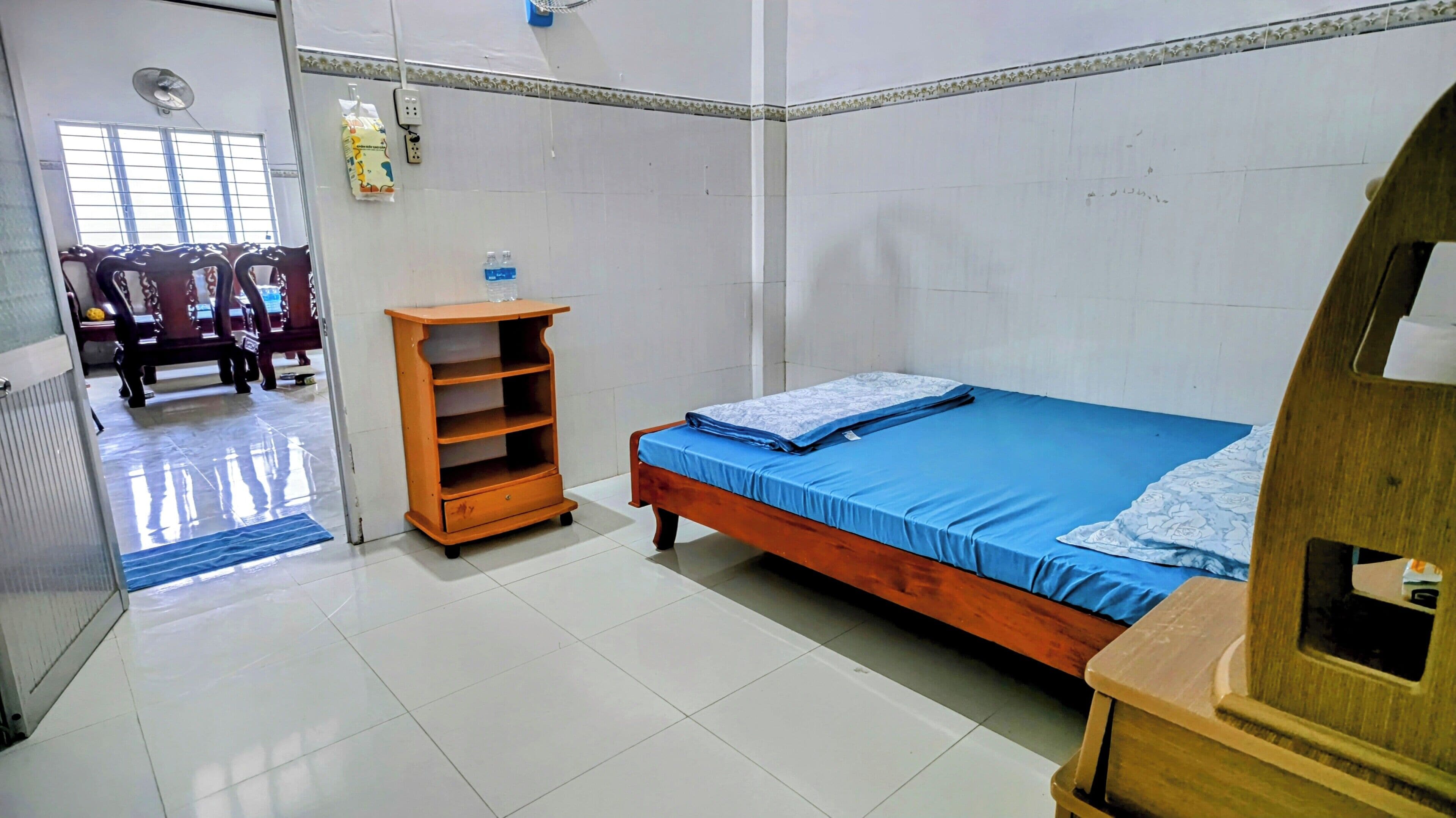 A bedroom with a bed, a wooden nightstand, a shelf unit, and a chair.
