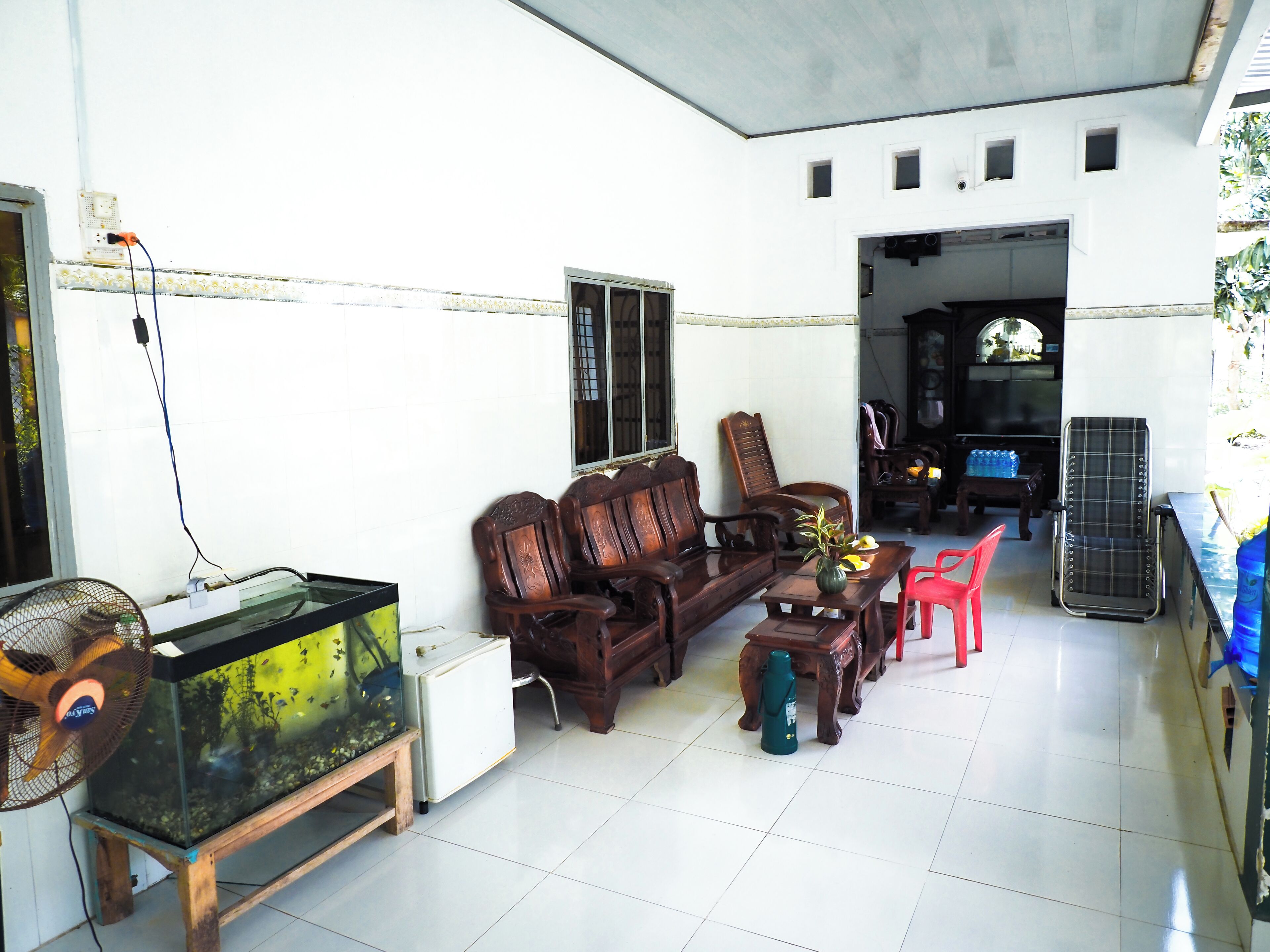 A living room with a wooden sofa, a red chair, a fish tank, and a fan.