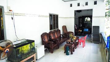 A living room with a wooden sofa, a red chair, a fish tank, and a fan.