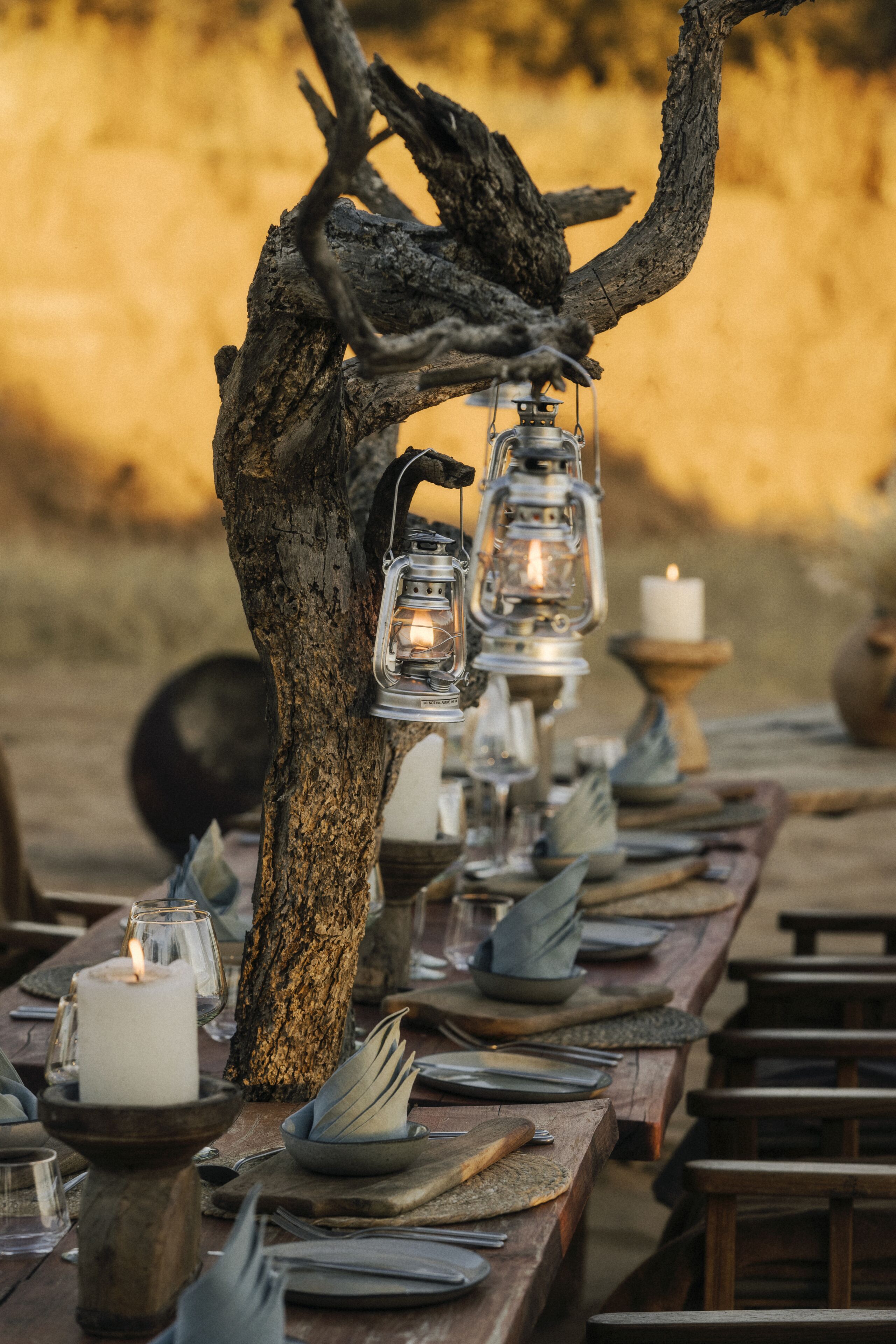 A dining table set with candles, lanterns, and neatly arranged plates and cutlery.