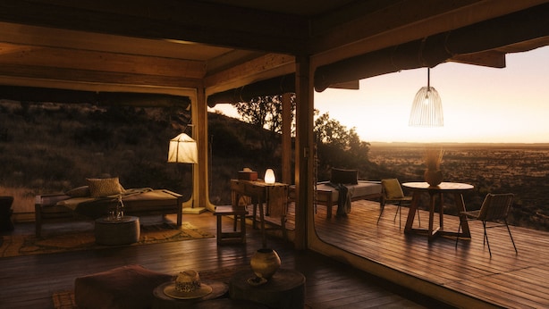 A cozy, open-plan living area with a wooden deck, a sofa, a table, and chairs. - Our Habitas Namibia (Windhoek)