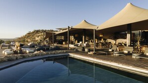 A poolside area with lounge chairs, umbrellas, and a wooden deck. - Our Habitas Namibia (Windhoek)