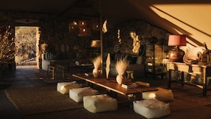A cozy, rustic interior with a stone wall, wooden furniture, and a large window. - Our Habitas Namibia (Windhoek)