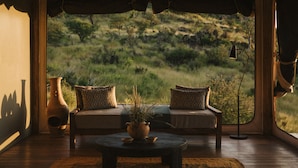 A room with a large window, a sofa with patterned cushions, a wooden table with a vase, and a floor lamp. - Our Habitas Namibia (Windhoek)