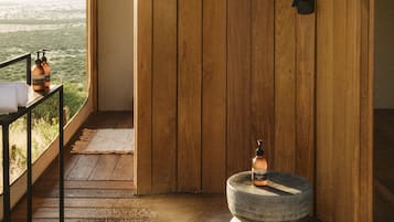 Relax in this serene bathroom with a showerhead, stool, and bench, offering a tranquil view of the lush landscape.