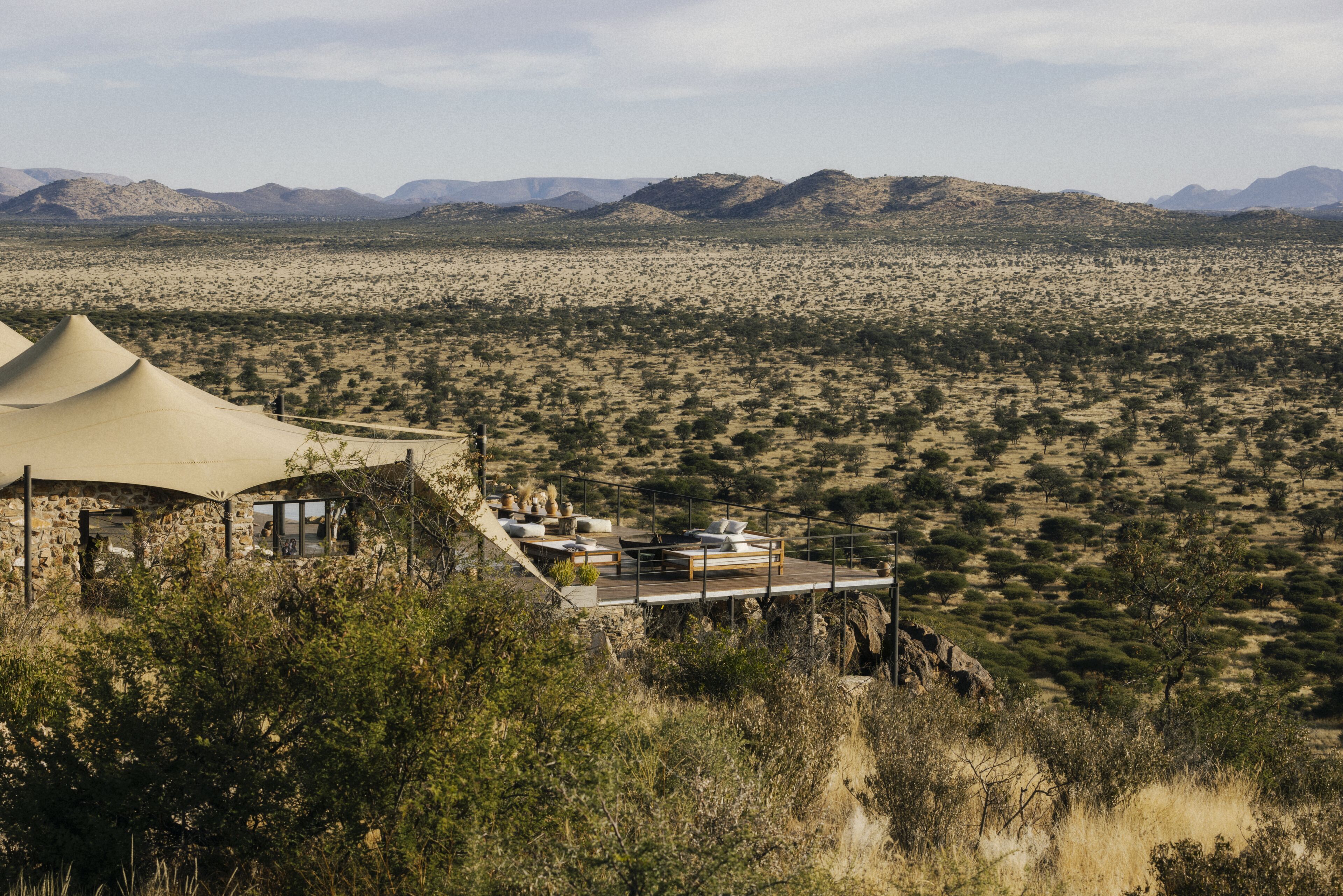 A desert landscape with a tented accommodation featuring a balcony with seating and a view of the surrounding desert.