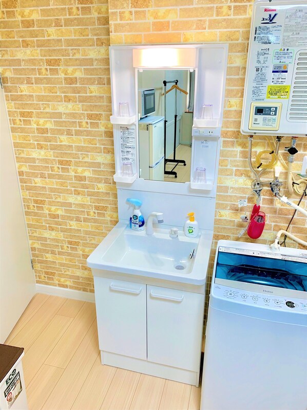 A bathroom with a white sink, mirror, and Haier washing machine. There are toiletries on the sink and a red cup holder on the wall. - Tanifuji A room (Sapporo)