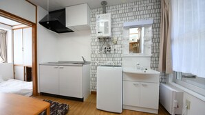 A compact hotel room with a kitchenette, a washing machine, a sink, and a bed.