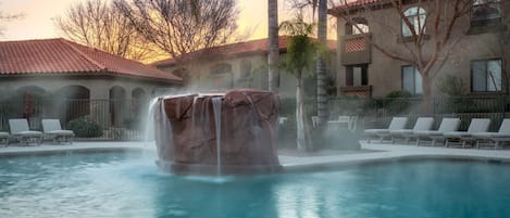 Relax by the serene pool surrounded by lounge chairs and a central waterfall feature.