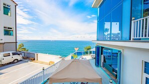 Un bâtiment moderne doté d’un balcon offrant une vue sur la côte, comprenant un coin repas et un espace salon abrité.