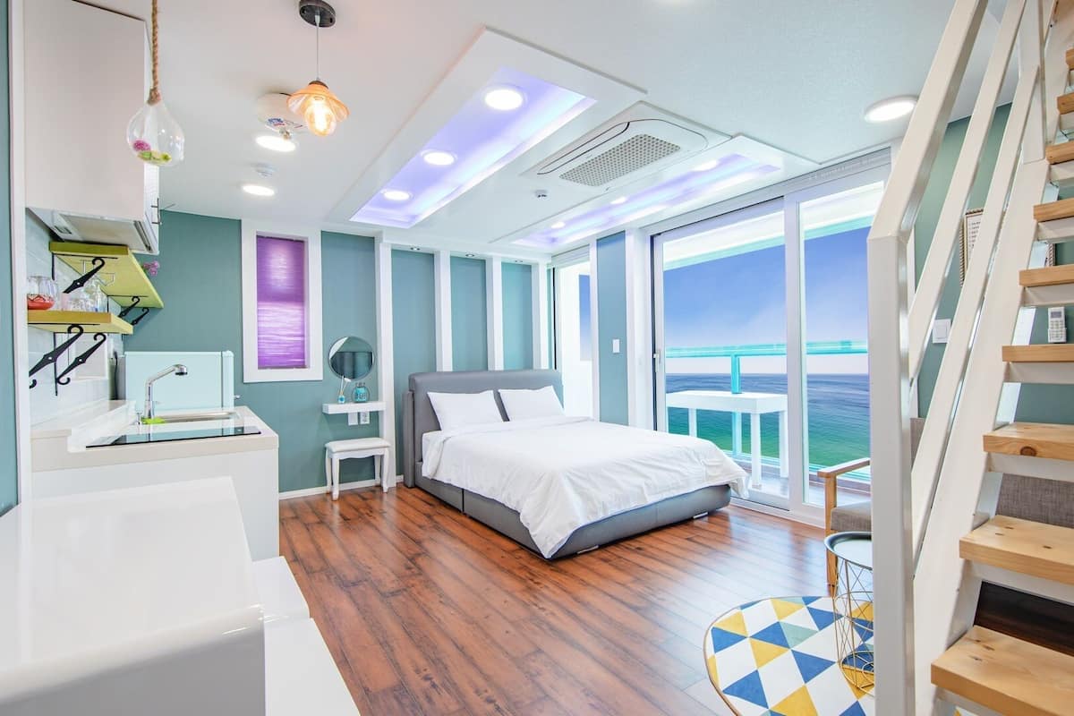 A modern bedroom with a large bed, a bathroom with a bathtub, and a view of the sea through large windows.
