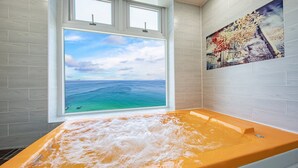 Une salle de bain avec une grande fenêtre, une baignoire et un tableau accroché au mur.