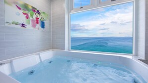 Une salle de bain avec une baignoire, une grande fenêtre donnant sur la mer et un mur orné d’une œuvre d’art florale.