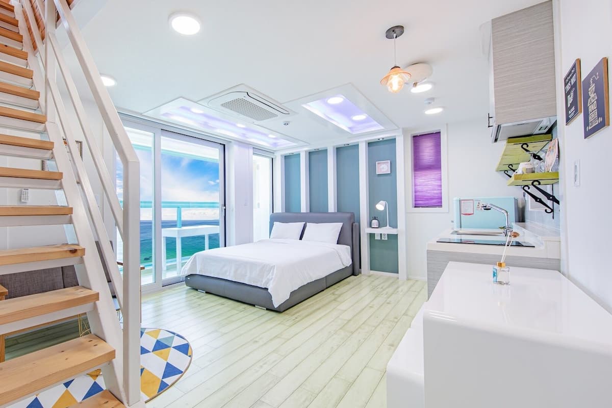 A modern bedroom with a large bed, a desk, and a staircase leading to an outdoor balcony.