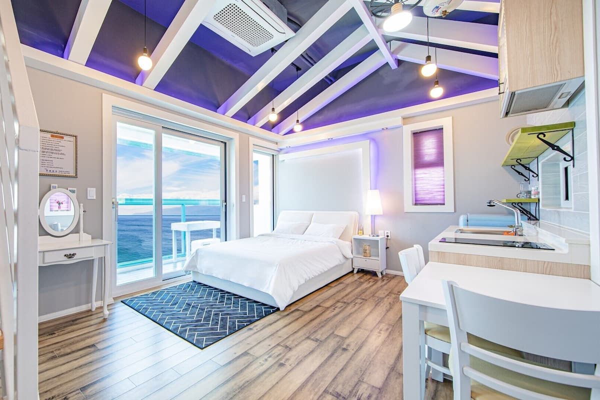 A modern bedroom with a large bed, a desk, and a view of the ocean.