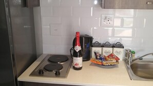 Une cuisine équipée d’une cuisinière à gaz, une bouteille de champagne et trois récipients étiquetés « sucre », « café » et « thé ».