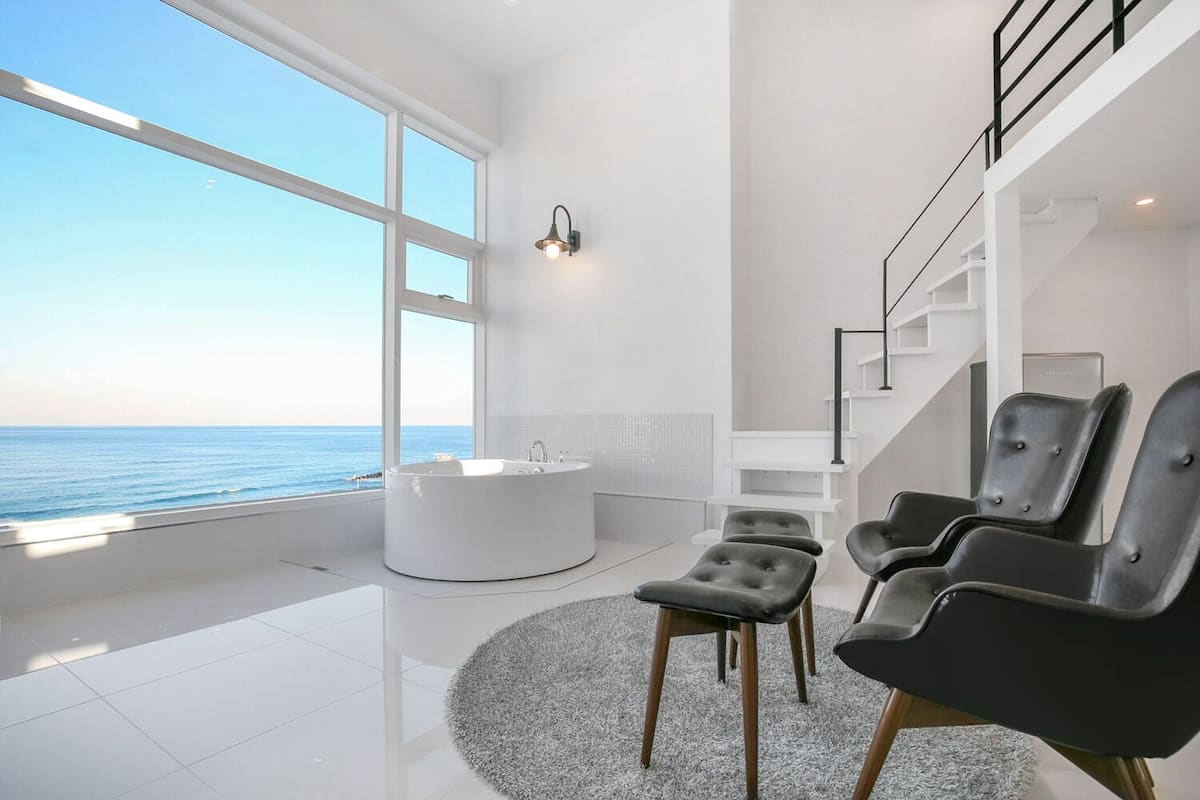 A modern bathroom with a large bathtub, a walk-in shower, and a view of the sea.
