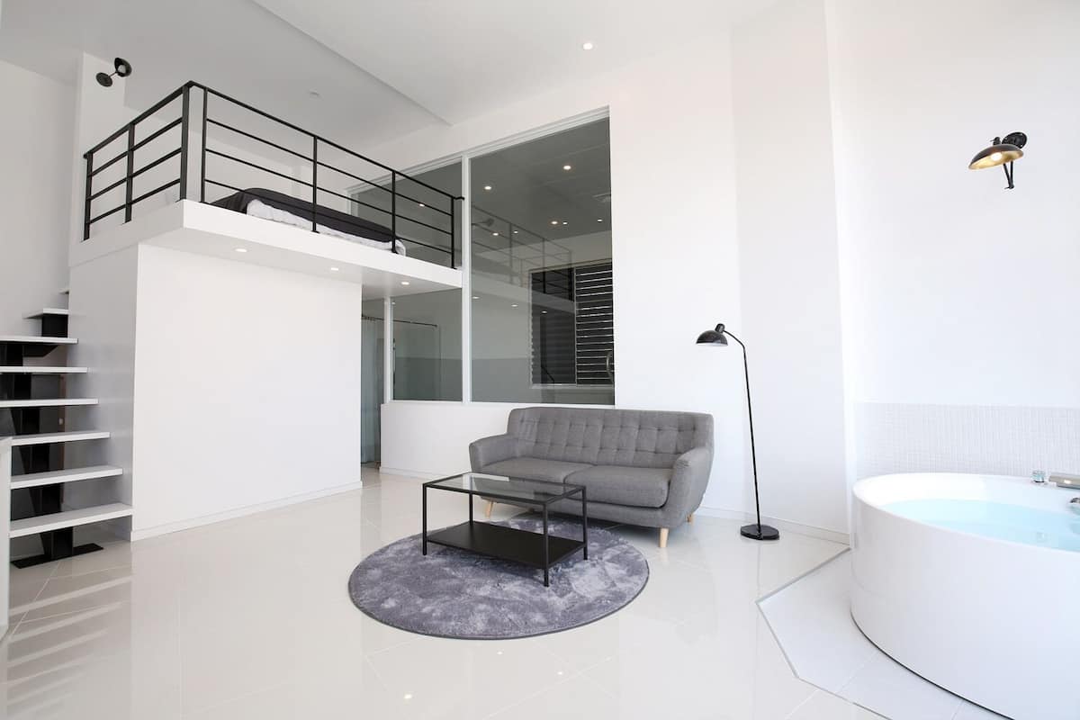A modern living room with a grey sofa, a glass coffee table, a black floor lamp, and a white bathtub.